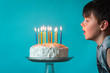 © Cavan Images - Boy ready to blow out candles on birthday cake against blue backdrop.