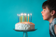 Boy Ready To Blow Out Candles On Birthday Cake Against Blue Backdrop.
