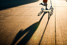 Lower Half Of Boy Scootering Fast In Sunlight With Shadow In Street