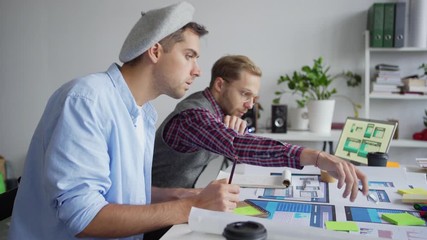 Wall Mural - Panning shot of two web designers creating application interface for different devices. Young professionals discussing samples and writing down ideas sitting at desk in office