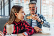 Stylish granddaughter. Cute stylish granddaughter wearing red shirt trying croissant having breakfast with grandfather.