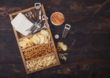 Glass Of Craft Lager Beer And Opener With Box Of Snacks On Wooden Background. Pretzel And Crisps And Salty Potato Sticks In Vintage Wooden Box With Openers And Beer Mats. Space For Text