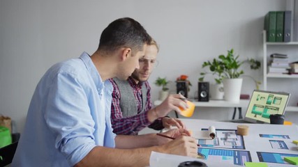 Wall Mural - Panning shot of two web designers working on application interface for various devices. Creative professionals discussing samples and writing down ideas on sticky notes sitting at desk in office