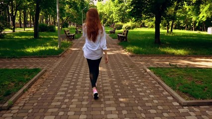 Poster - beautiful young woman talking by smartphone turn to the camera person with long red hair in white shirt walks in summer city green nature sunny day