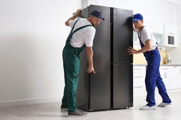 Wall Mural - Professional workers carrying modern refrigerator in kitchen