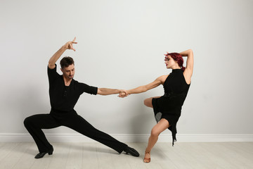 Beautiful young couple dancing near light wall