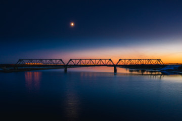 Aerial view on railroad bridge at sunset with moving cars. Steel construction silhouette on a colorful sky background. 