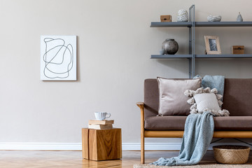 Stylish interior design of living room at cozy apartment with brown sofa, gray bookstand, wooden cube with tea cup and elegant accessories. Mock up poster frames on the wal. Home staging Beige concept