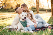 © zadorozhna - Happy beautiful family with dog labrador is having fun  are sitting on green grass in park.