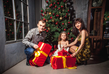 family mom dad and daughter at the Christmas tree with gifts