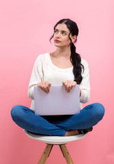 Wall Mural - Young woman with a laptop computer in a thoughtful pose on a pink background