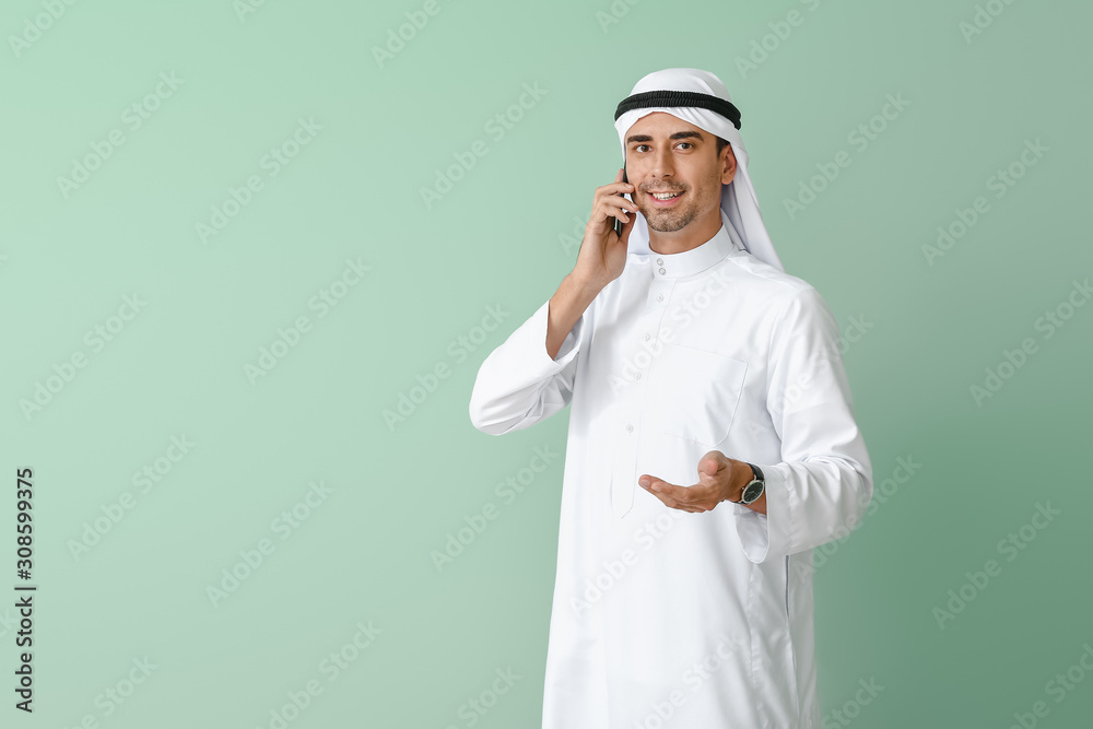Handsome Arab man talking by phone on color background