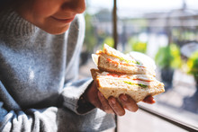 Closeup image of a woman holding and eating whole wheat sandwich in the morning