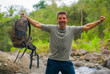 © TheVisualsYouNeed - young happy and attractive man with travel backpack hiking in river at forest feeling free enjoying nature and fresh environment on summer trekking journey