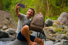 Young Happy And Attractive Man Taking Selfie With Mobile Phone Holding Backpack Hiking In River At Forest Enjoying Nature Carefree On Summer Trekking Journey