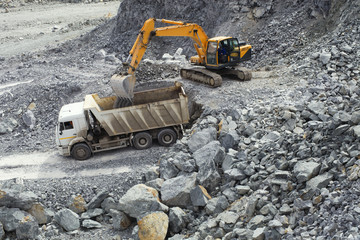 Excavator loads ore into the body of a dump truck in a stone quarry.
