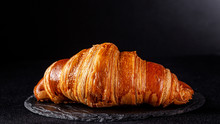 French Cuisine Concept. French Croissant From Puff Pastry Dough Lies On A Black Slate Board, On A Black Background. Copy Space