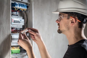 Wall Mural - Man, an electrical technician working in a switchboard with fuses. Installation and connection of electrical equipment.