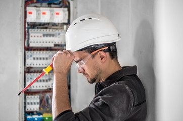 Wall Mural - Man, an electrical technician working in a switchboard with fuses. Installation and connection of electrical equipment.