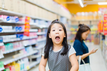 Wall Mural - Surprised and excited face of happy little asian girl in supermarket with mom.Little girl open mouth in hypermarket with family.wow emotion in kid.