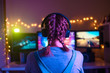 © Anton - Gamer or streamer girl at home in a dark room playing video games with friends online. A young man sits in front of three monitors