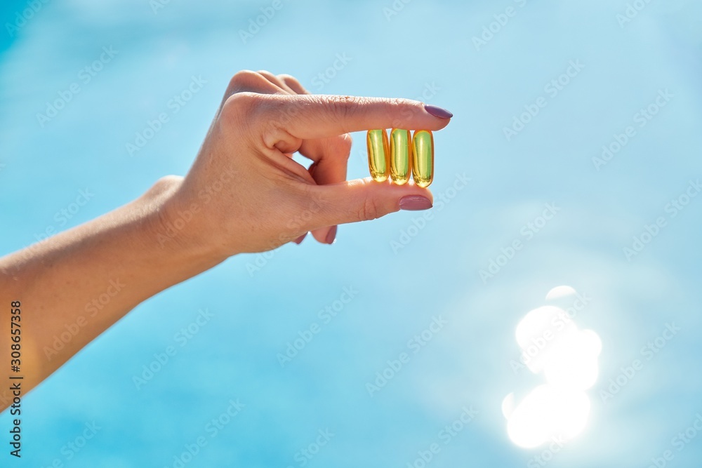 Obraz na płótnie Sunny golden vitamin D oil capsules Omega-3 in woman hand w salonie
