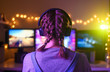 © Anton - Gamer or streamer girl at home in a dark room playing video games with friends online. A young man sits in front of three monitors