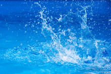 Splashes Of Clear Blue Fresh Water In Pool, Air Bubbles, Water Drops, Sea Wave On Blue Background With Sunny Reflections.