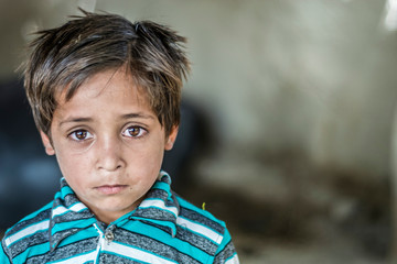 Wall Mural - closeup of a poor staring hungry orphan boy in a refugee camp with sad expression on his face and his face and clothes are dirty and his eyes are full of pain