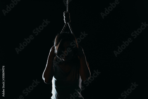 Fotografía depressed woman committing suicide while putting noose on neck in darkness isola