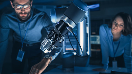 Leinwandbilder - Close Up of a Futuristic Robotic Arm Picking Up a Metal Object and Moving It. Team of Engineers Following This Advanced Process. They are in a High Tech Research Laboratory with Modern Equipment.
