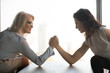 Side view mature and young businesswomen arm wrestling, confrontation