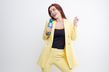 Wall Mural - Red-haired girl in a yellow suit sings into a microphone on a white background