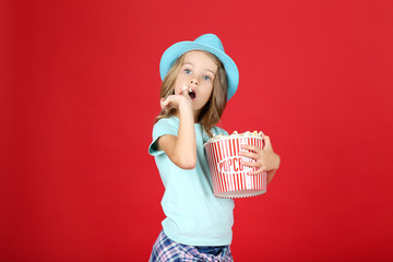 Wall Mural - Young girl with popcorn in bucket on red background