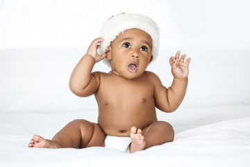 Wall Mural - American baby girl in santa hat sitting on white bed