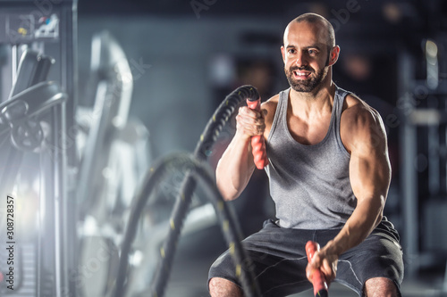 Fotomural Muscular man exercising with battle ropes at the fitness gym