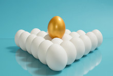 Concept Of Individuality, Exclusivity, Better Choice. One Golden Egg Among White Eggs On Blue Background.