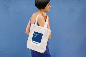 Wall Mural - Woman holding canvas tote bag on bright blue background in the city. Reusable eco bag. Classic Blue. Color of the year 2020. 