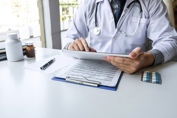 Doctor working and using digital tablet note information on paper report in hospital and medical stethoscope, medicine on clipboard on desk