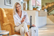 © Kalim - Businesswoman with luggage in modern hotel lobby using smartphone