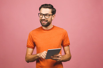 Wall Mural - Happy young man in casual standing and using tablet isolated over pink background.
