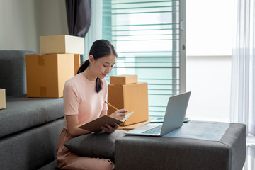 Wall Mural - Asian woman student and small businesses online working at home taking note the customer order.