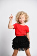 Smiling kid girl in fatin skirt and t-shirt is holding her hand up pointing pushing the button with her finger on white