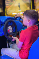 Wall Mural - Cute European boy in red t-shirt playing car racing on slot-machine. He enjoying his spare time