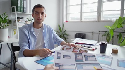 Wall Mural - POV of two entrepreneurs discussing mobile application interface samples for different devices printed on paper sitting at desk in office