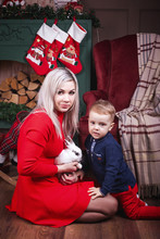 Beautiful Mother With Cute Child Boy Sitting Holding White Rabbit. Christmas Stocking Wood And Decorations On The Background. Concept Of Happy Christmas Holiday