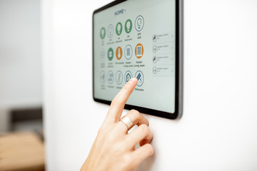 Wall Mural - Controlling home with a digital touch screen panel installed on the wall. Close-up on a screen with mobile application for managing smart devices