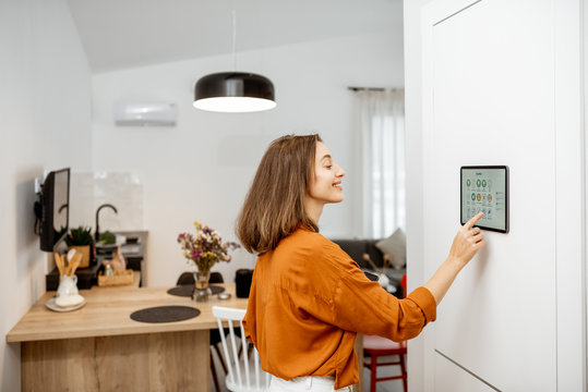 young woman controlling home with a digital touch screen panel installed on the wall in the living r