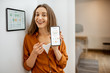 © rh2010 - Portrait of a young and happy woman near a touch screen panel for managing smart home. Holding smart phone with a simlpe and convinient mobile application for smart home
