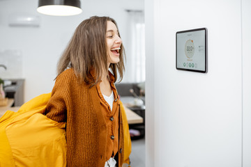 Wall Mural - Happy woman taking off her outerwear by coming to a warm home. Concept of a smart home and remote heating control over the internet